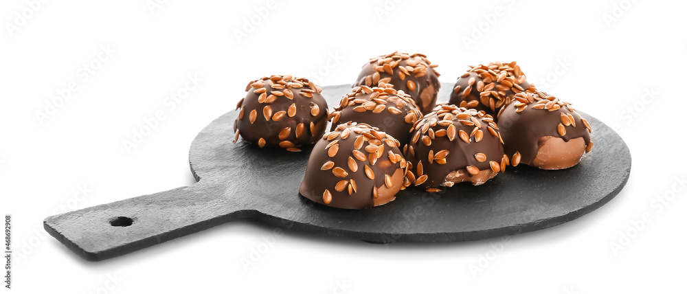 Board with tasty flax seed candies on white background