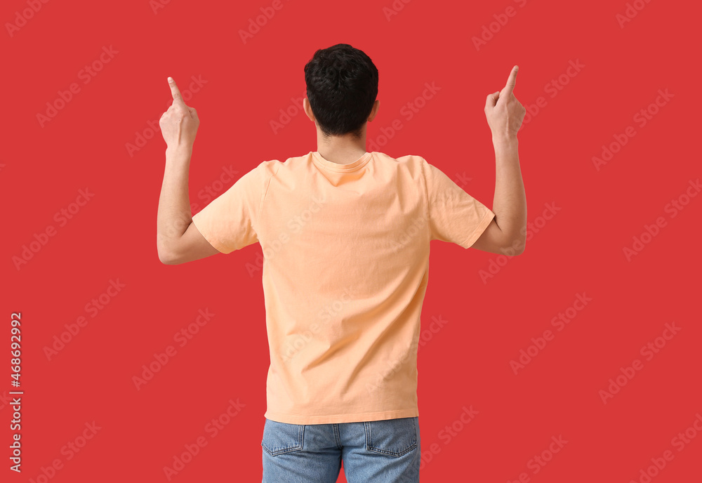 Handsome young man in stylish t-shirt pointing at something on color background, back view