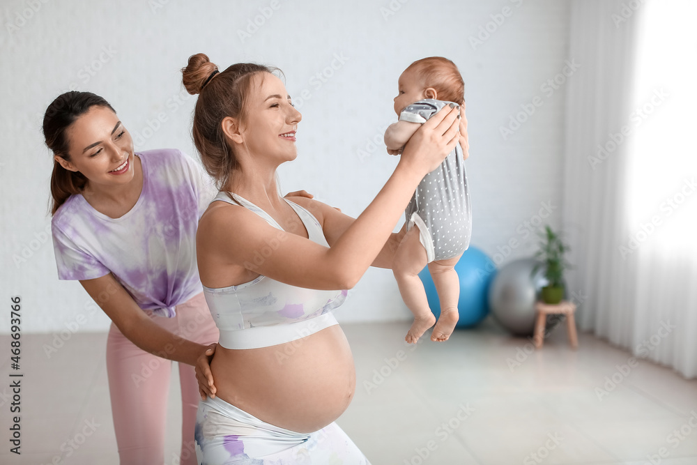 年轻孕妇带着小婴儿和教练在健身房做瑜伽