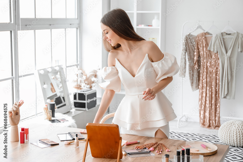 Pretty young woman near table with decorative cosmetics in dressing room