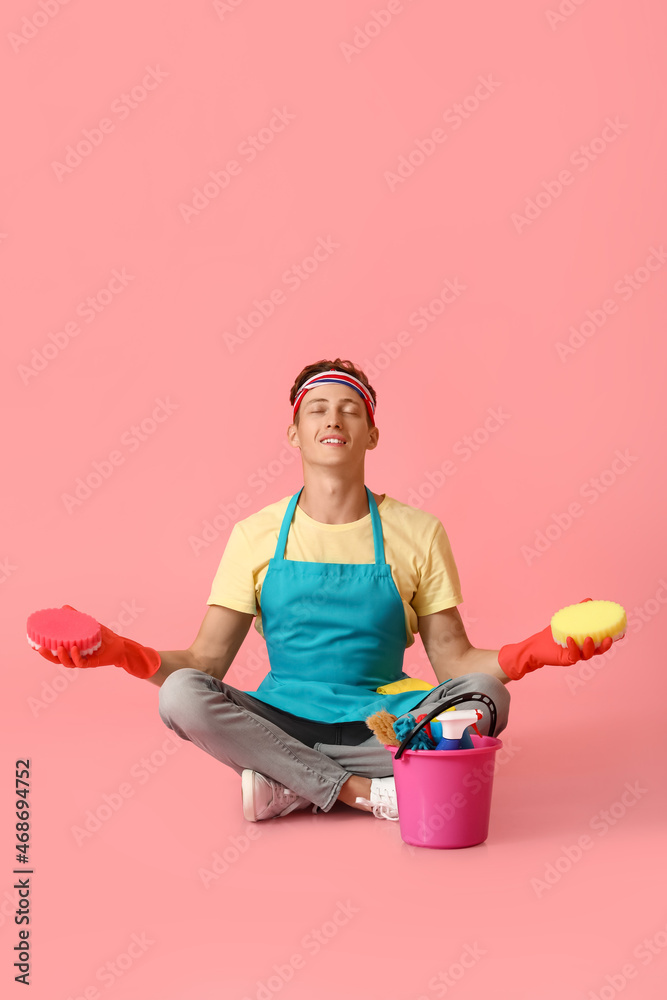 Handsome man with cleaning sponges meditating on pink background