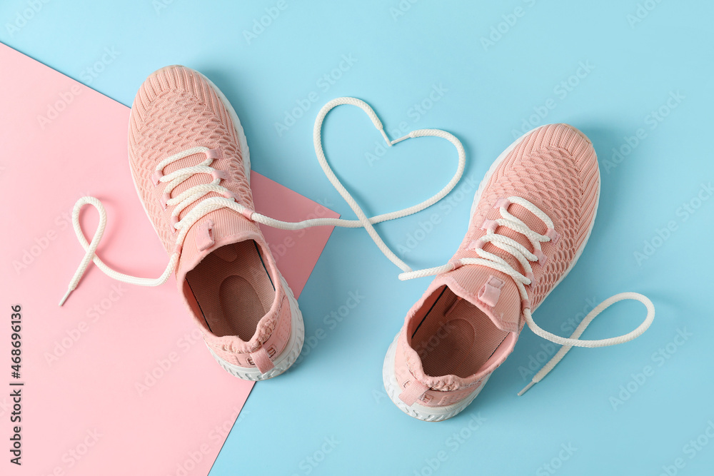 Pair of sportive shoes and heart made of laces on color background