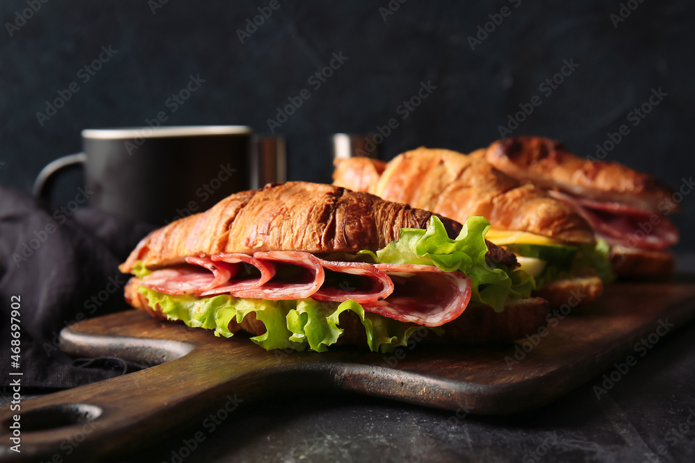 Wooden board with delicious croissant sandwiches on black background