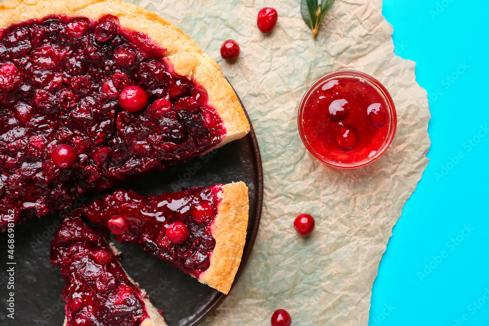 Plate with cut tasty lingonberry pie and jam on color background