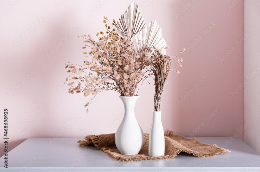 Vases with beautiful dried flowers on table near light wall