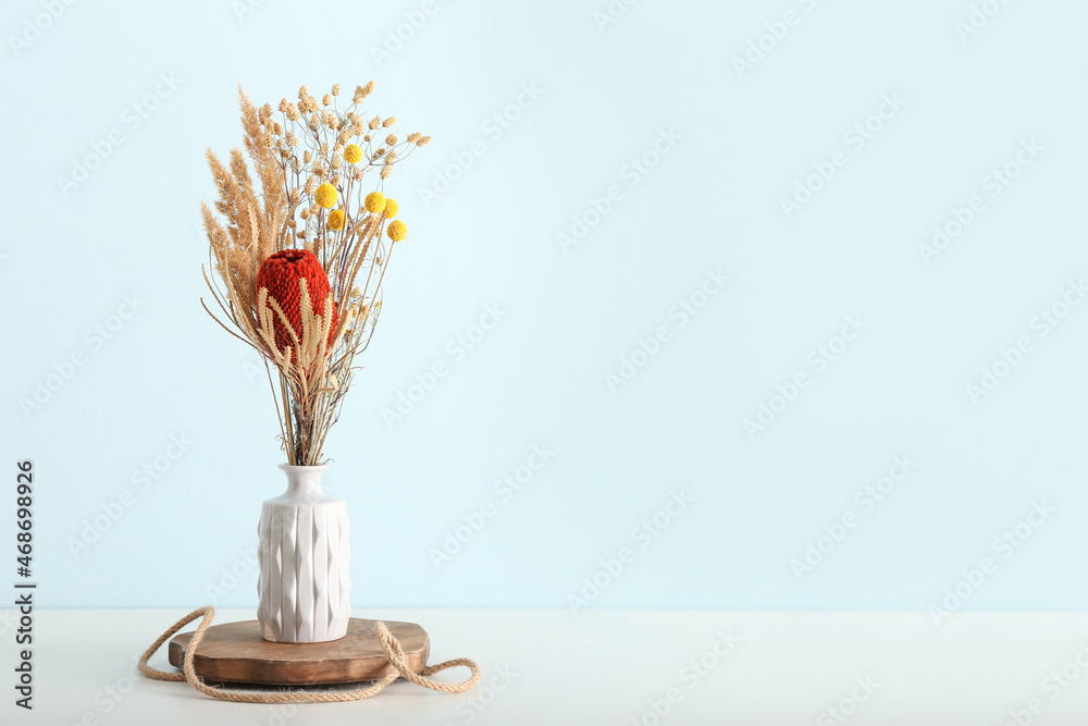 Vase with beautiful dried flowers on table near blue wall