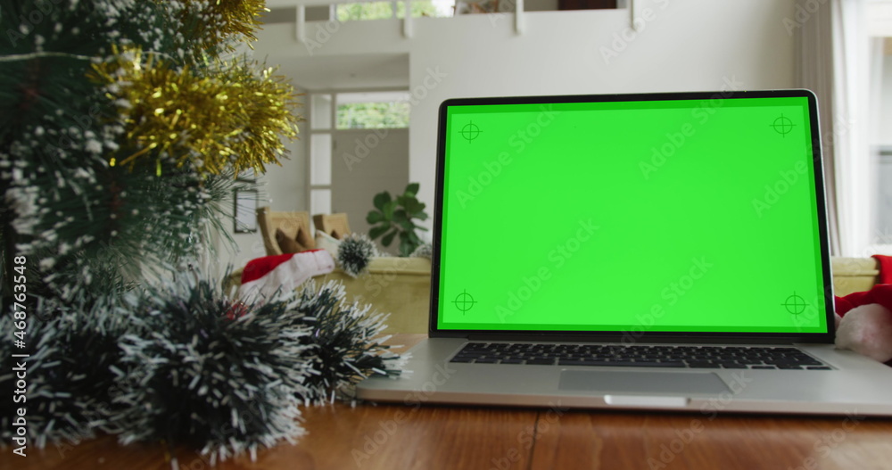 Laptop with green screen copy space on table at home, with decorated christmas tree