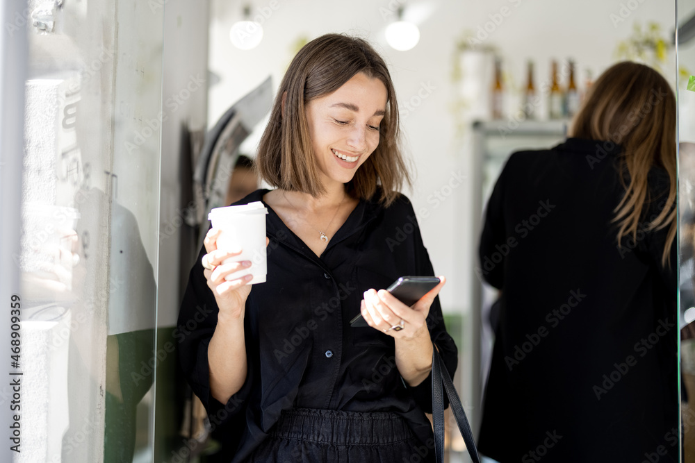 年轻的高加索女性，在咖啡馆或商店里拿着智能手机和咖啡。现代成功的概念