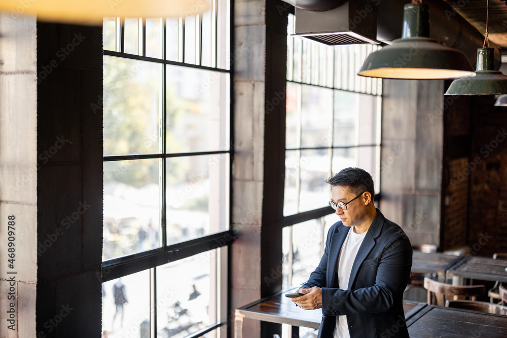 Asian businessman talking on mobile phone standing near window in cafe. Concept of remote and freela