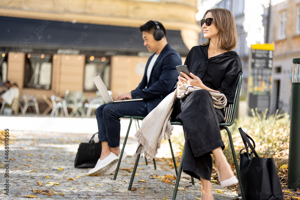 Two businesspersons sitting separately on chairs on the old city street outdoors. Concept of city li