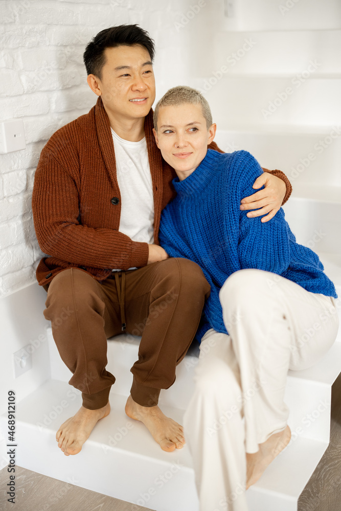 Asian man hugging his young caucasian wife on stairs at home. Concept of relationship and spending t