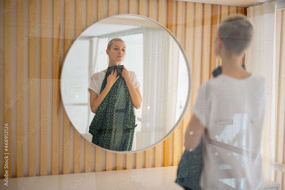 Young caucasian woman looking green dress with dots on herself in mirror. Concept of fashion. Back v