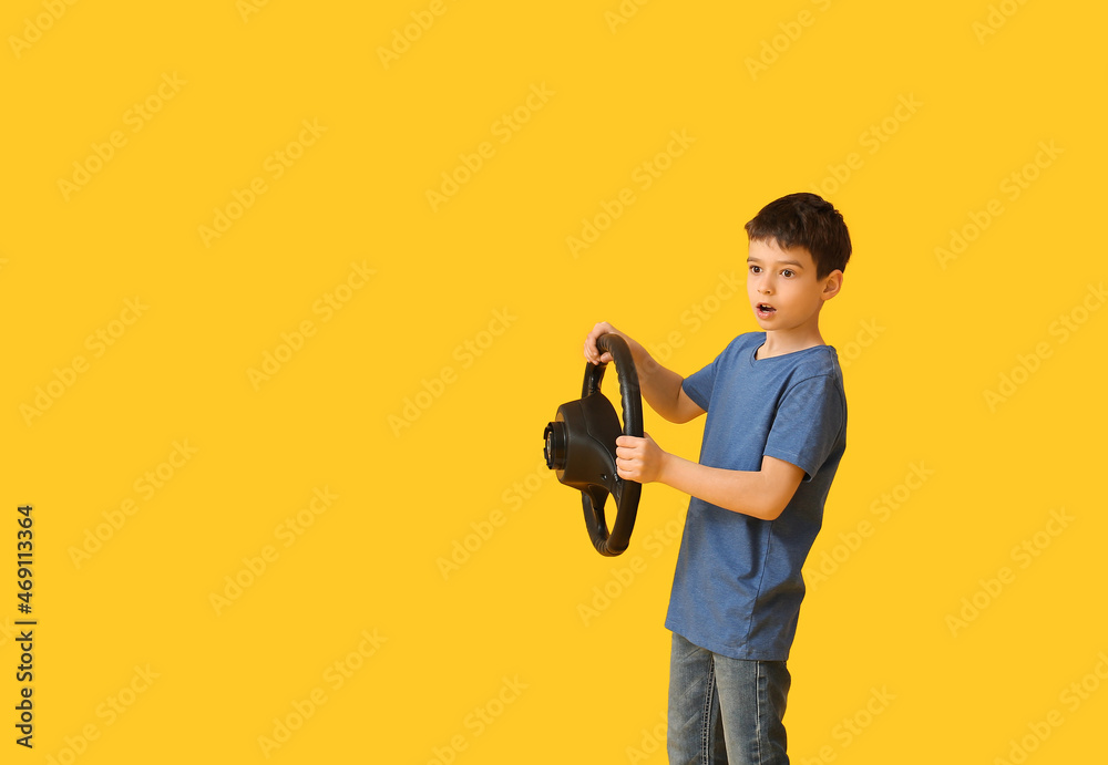 Shocked little boy with steering wheel on color background