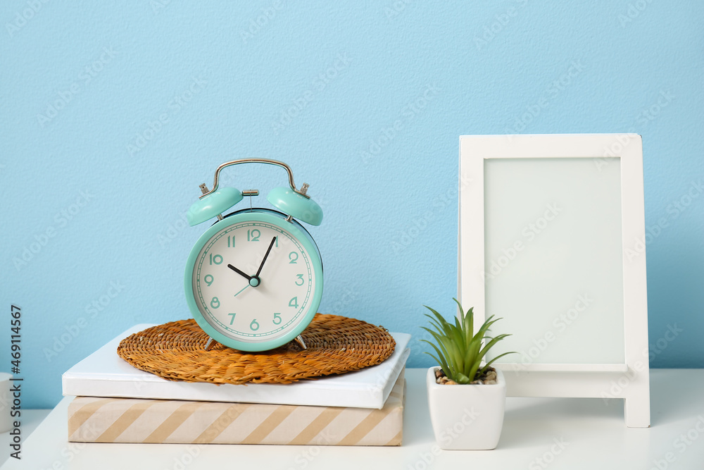 Alarm clock, books, houseplant and frame on table in room, closeup