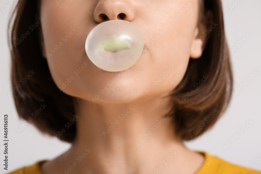 Young woman with chewing gum on light background, closeup