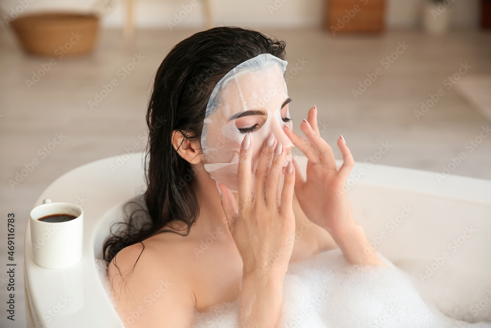 Pretty young woman with sheet facial mask taking bath at home