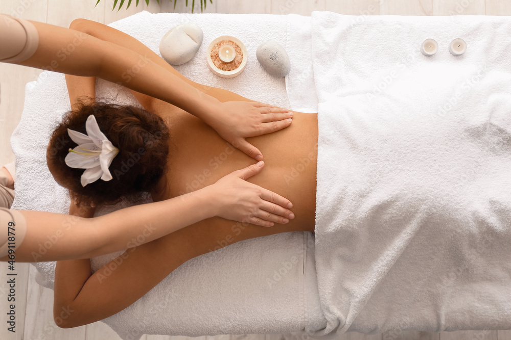 Relaxed African-American woman getting massage by therapist in spa salon