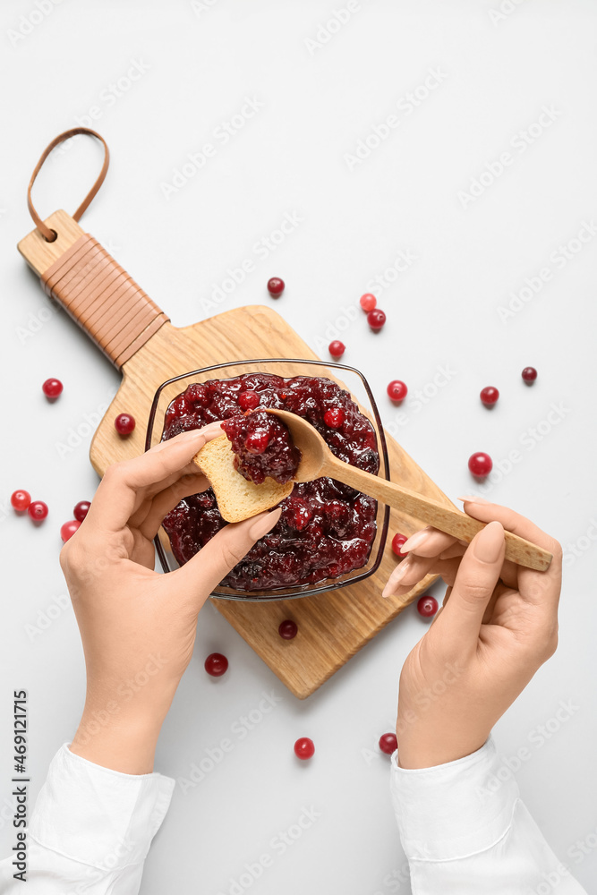 Woman preparing tasty sandwich with cranberry jam on light background