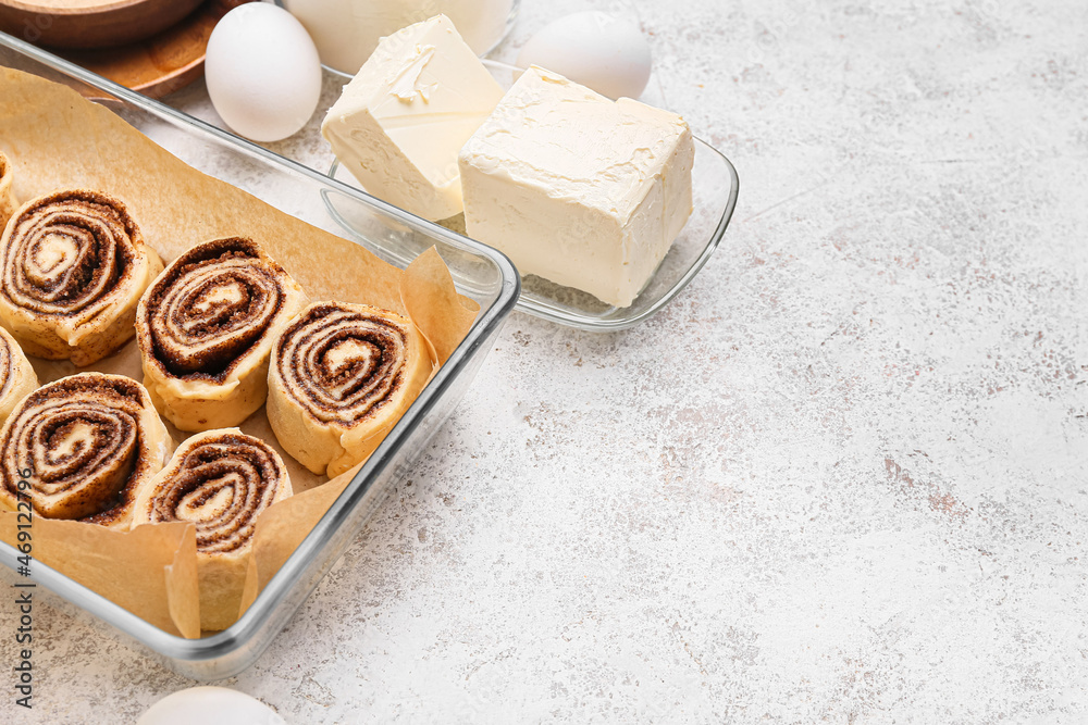 Baking dish of uncooked cinnamon rolls and butter on white background, closeup