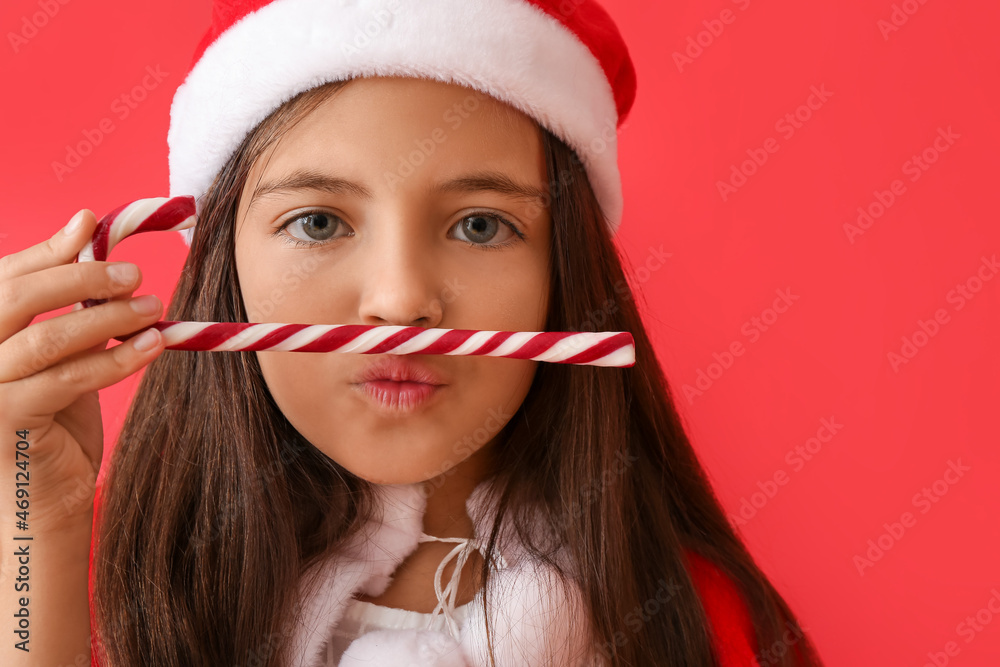 Cute little girl in Santa hat and with candy cane on color background