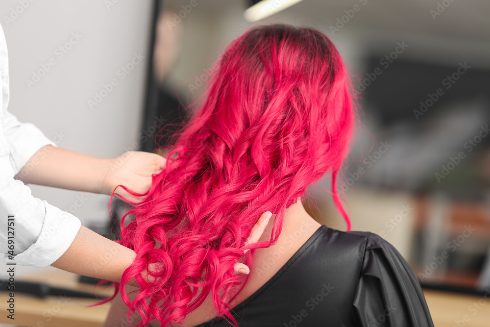 Stylist doing hair of young woman in beauty salon