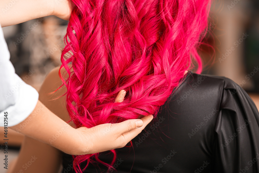 Stylist doing hair of young woman in beauty salon