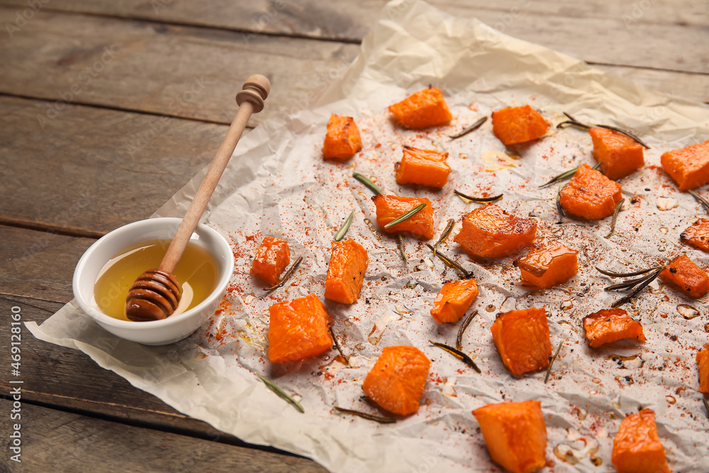 Parchment with tasty roasted pumpkin pieces on wooden background