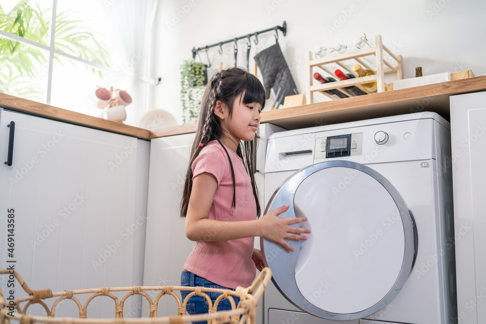 亚洲小孩把脏衣服放进屋里的洗衣机里。