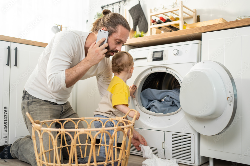 Caucasian busy father doing housework with baby boy toddler in kitchen. 