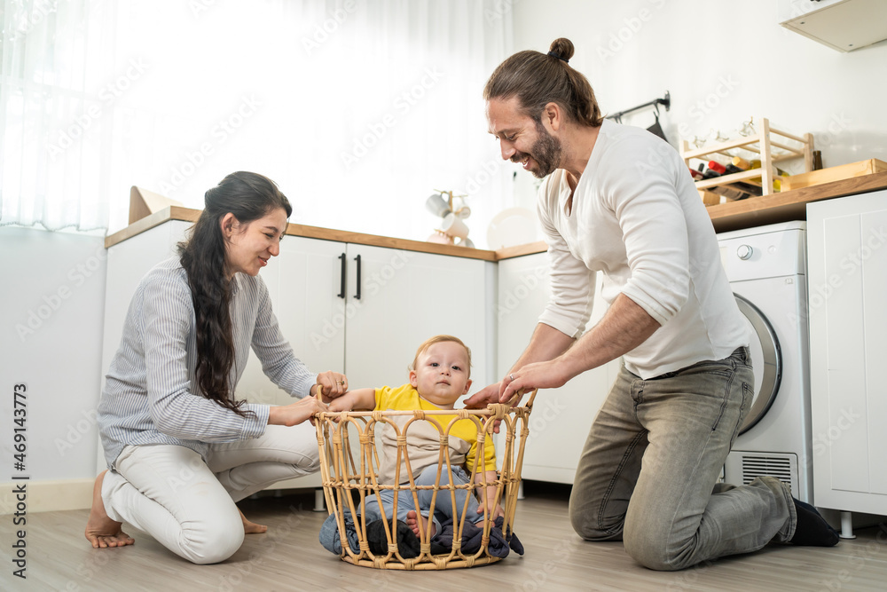 Caucasian loving parents play with baby toddler in kitchen on floor.