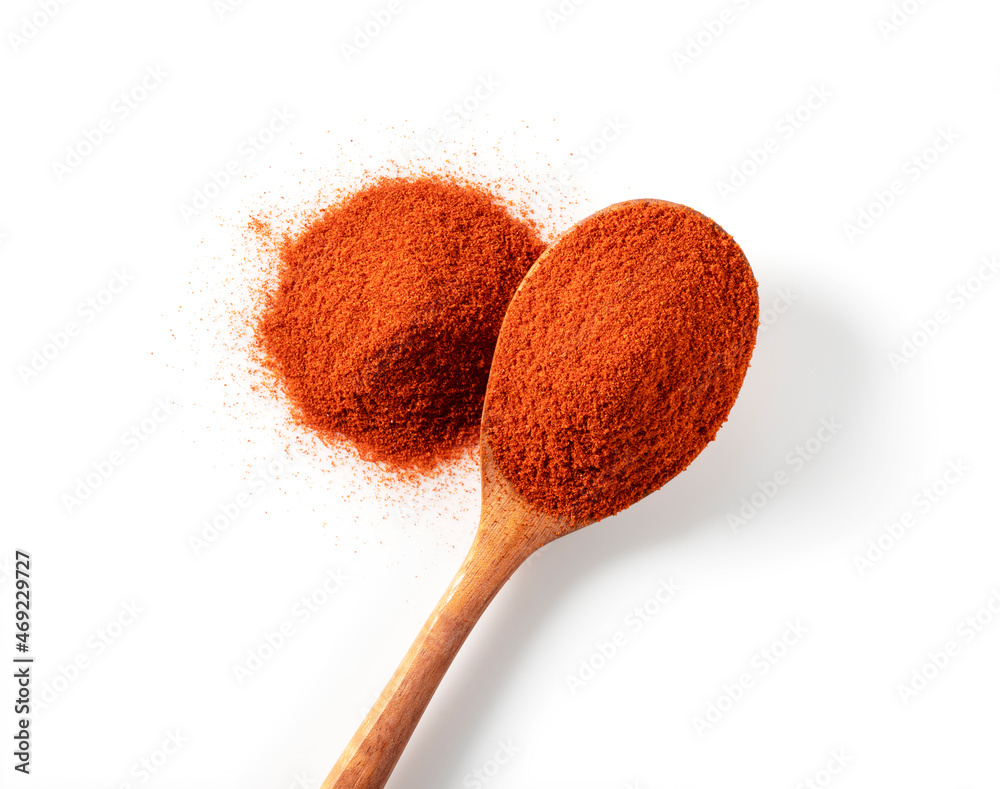 Red pepper powder and wooden spoon on a white background