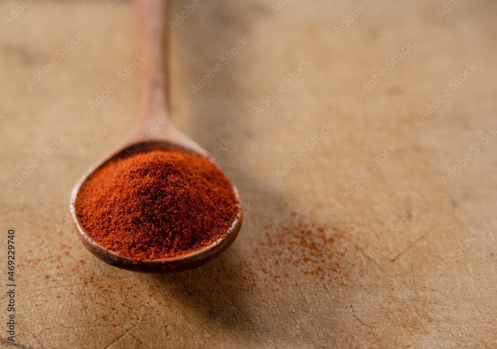 Red pepper powder and wooden spoon placed on a wooden background.