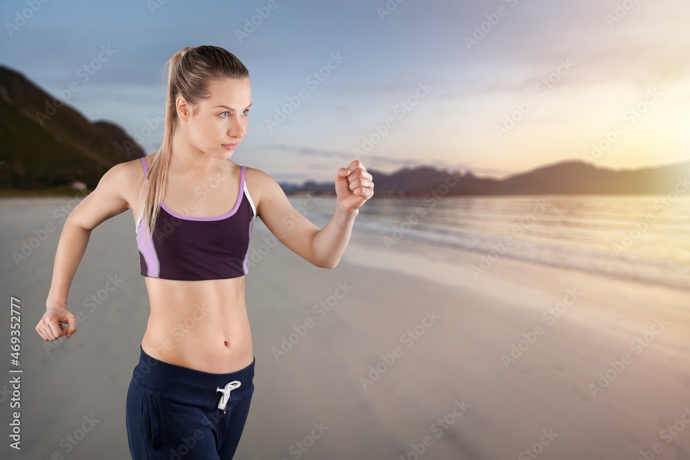 Happy young woman in sportswear jogging on beach.