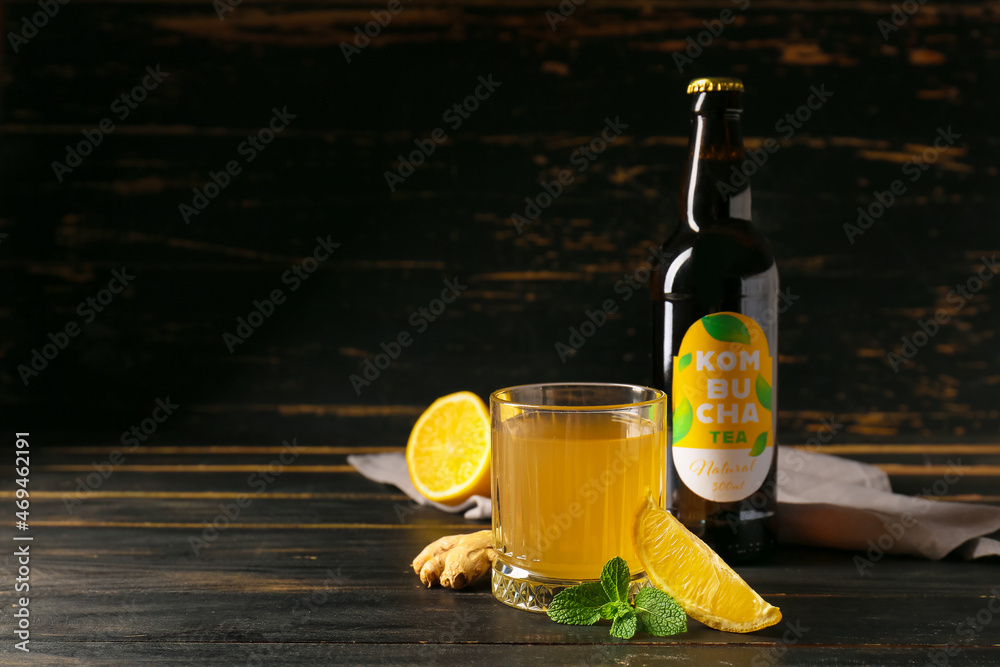 Bottle and glass of fresh kombucha on dark wooden table