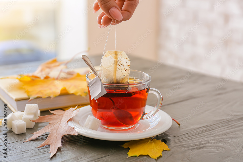 Female hand dipping tea bag in hot water at table in cafe