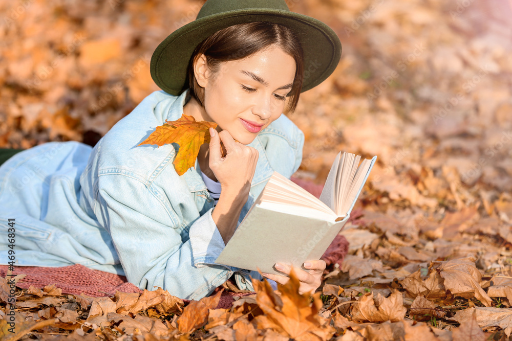 Portrait of woman with autumn leaf and book in park