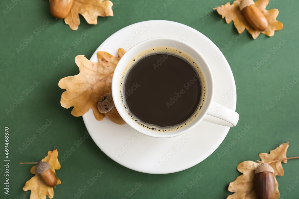 Cup of coffee with acorns and autumn leaves on green background