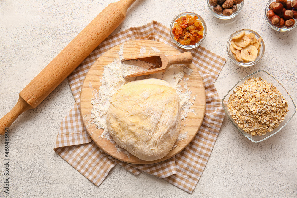 Wooden board with fresh dough and ingredients for preparing homemade cookies on light background