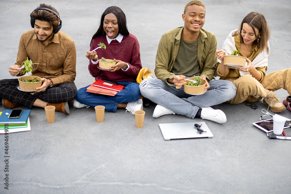 Multiracial students sitting and eating salad during lunch on asphalt at university campus. Concept 