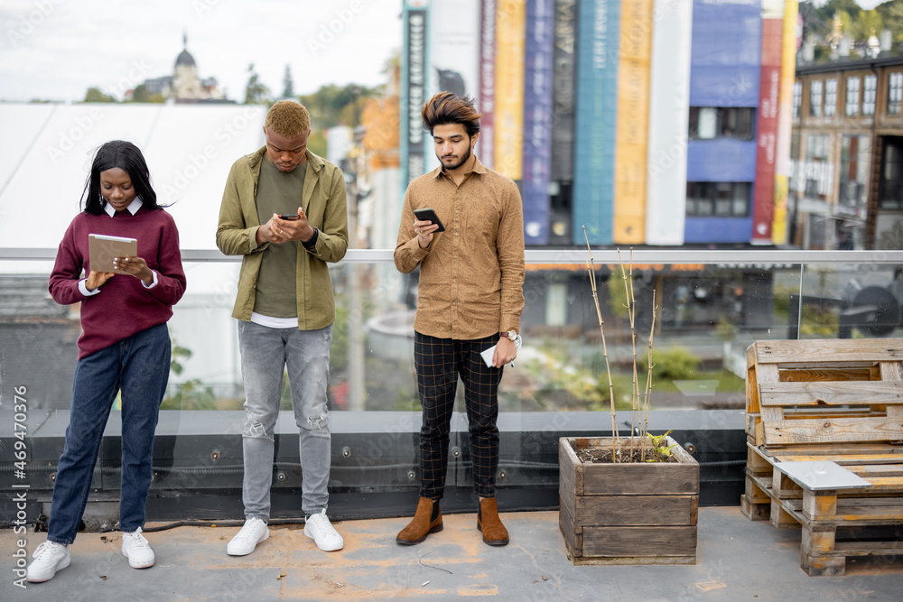 Focused multiracial students using digital devices on balcony at university campus. Concept of educa