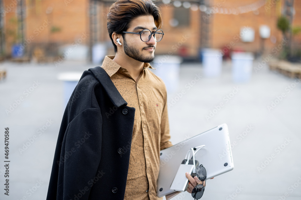 Young indian man with gadgets looking at camera outdoors. Handsome smiling stylish guy in glasses. C