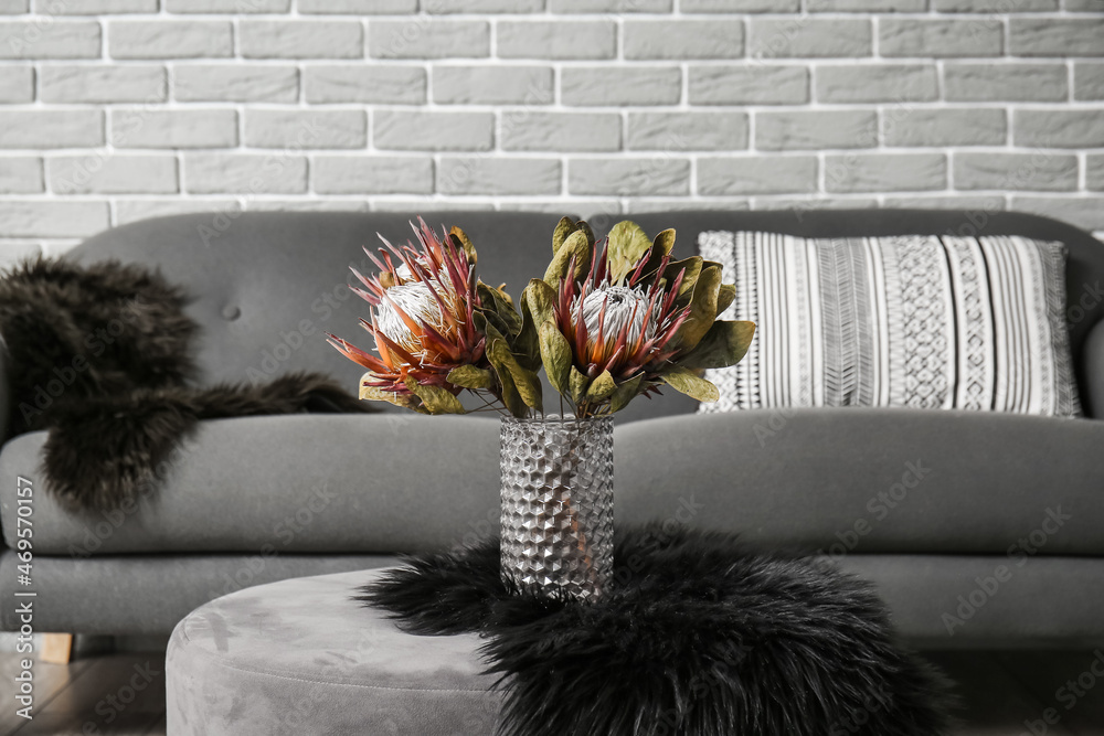 Stylish interior with grey sofa and flowers on brick wall background