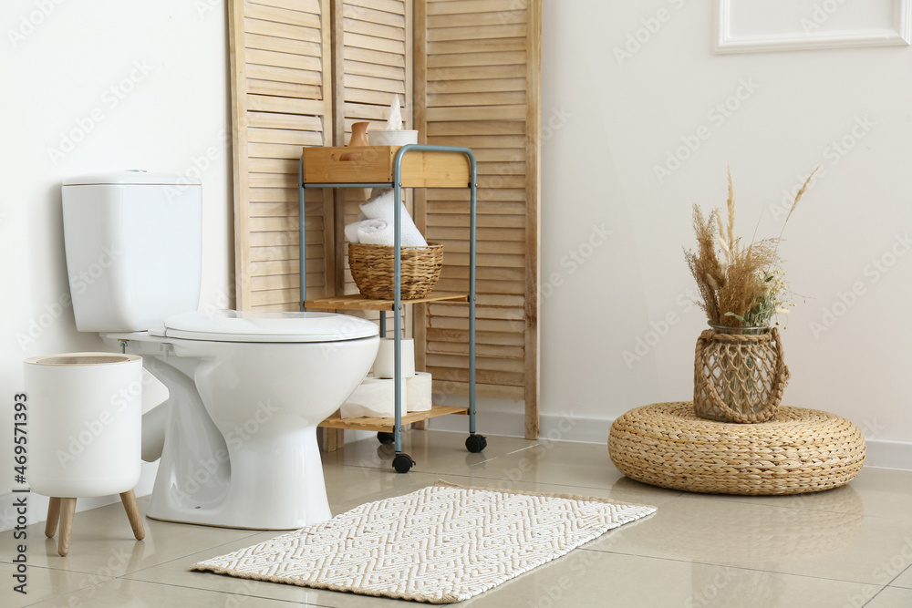 Interior of light restroom with toilet bowl and shelving unit