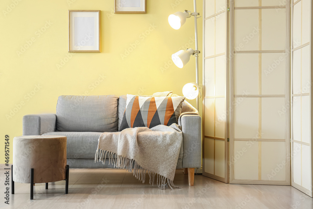 Folding screen with glowing lamp and sofa near yellow wall