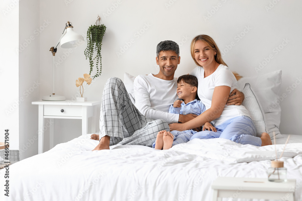 Happy parents with their little son sitting on bed