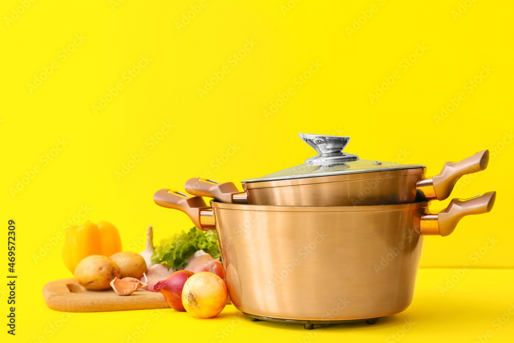 Fresh vegetables and cooking pots on color background