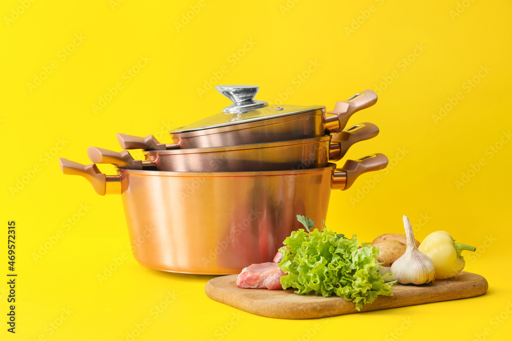 Fresh vegetables and cooking pots on color background