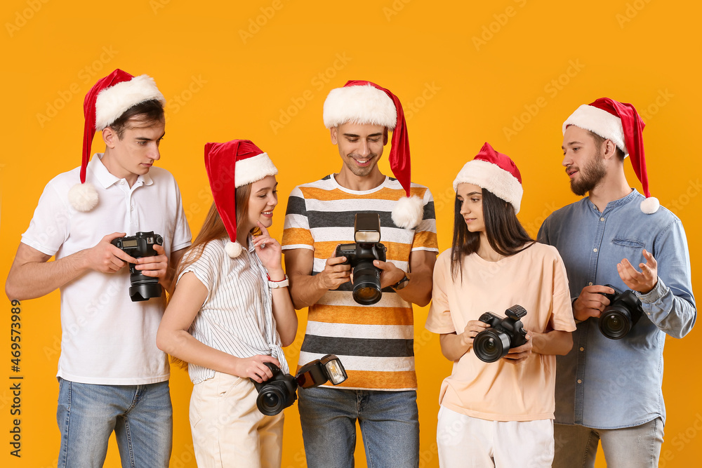 Group of photographers in Santa Claus hats on color background