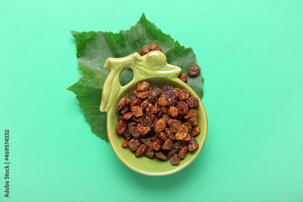 Bowl with tasty raisins on green background