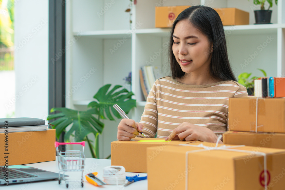 Young asian woman startup small business freelance sitting with parcel box and computer laptop on wo